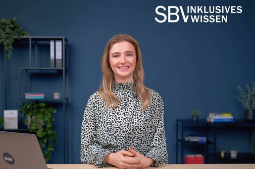 Klim Blum im Studio, sie lacht in die Kamera, im Hintergrund sind Büromöbel zu sehen, rechts im Bild das Logo SBV Inklusives Wissen
