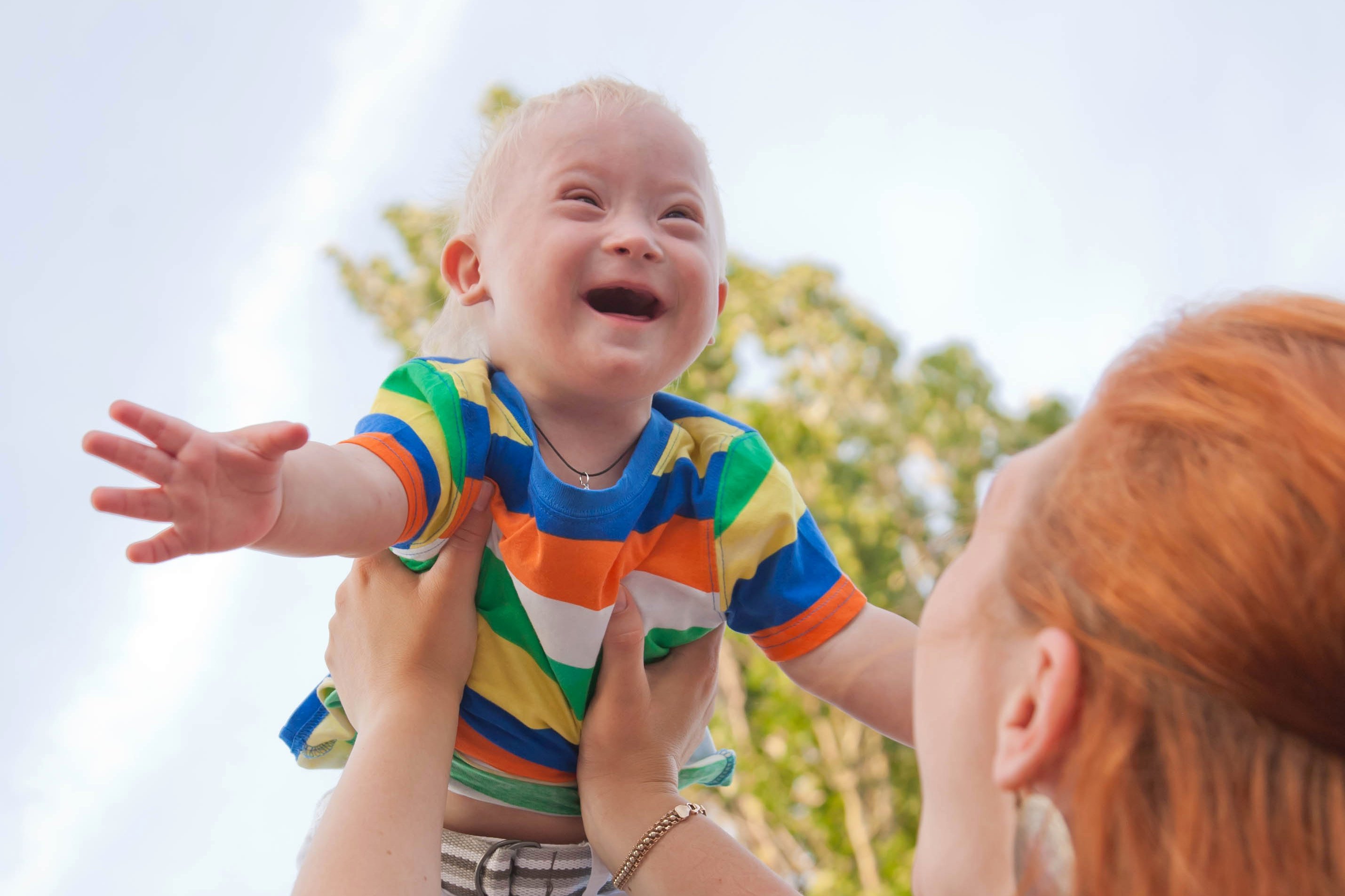 Baby mit Down-Syndrom lacht glücklich, als seine Mutter es in die Luft hebt