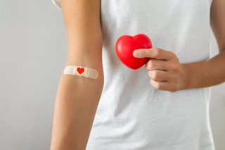 Impfung Symbolbild, junge Frau mit einem roten Herzen in der Hand und einem Pflaster im Handgelenk