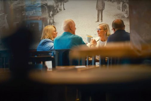 Blick im Innenraum auf eine Gruppe von Menschen, diese sitzen an einem Tisch und sind in ein Gespräch vertieft.