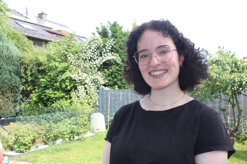 Portraitaufnahme von Nicole Zierat, im Hintergrund ist ein garten zu sehen, sie lacht in die Kamera
