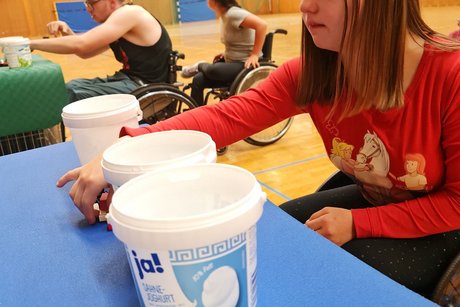 Mädchen im Rollstuhl beim Geschicklichkeitsspiel mit einem Joghurt-Becher