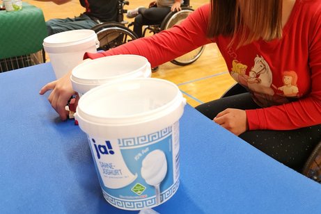 Mädchen im Rollstuhl beim Geschicklichkeitsspiel mit einem Joghurt-Becher