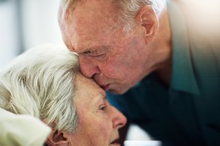 Senior küsst seine Frau die auf dem Bett liegt auf die Stirn