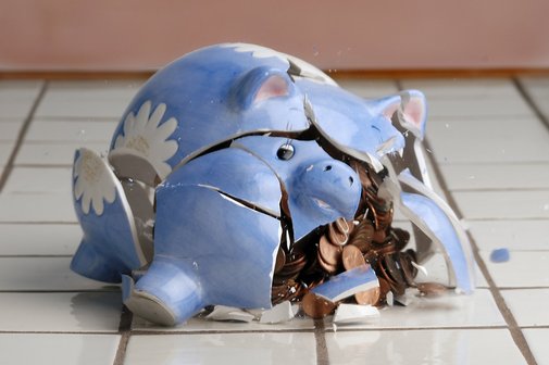 Ein blaues Sparschein, prall gef&uuml;llt mit M&uuml;nzen, das zerbrochen am Boden liegt.