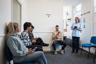 Wartezimmer beim Arzt Patienten sitzen auf Stühlen und starren aufs Handy Schwester ruft jemanden auf