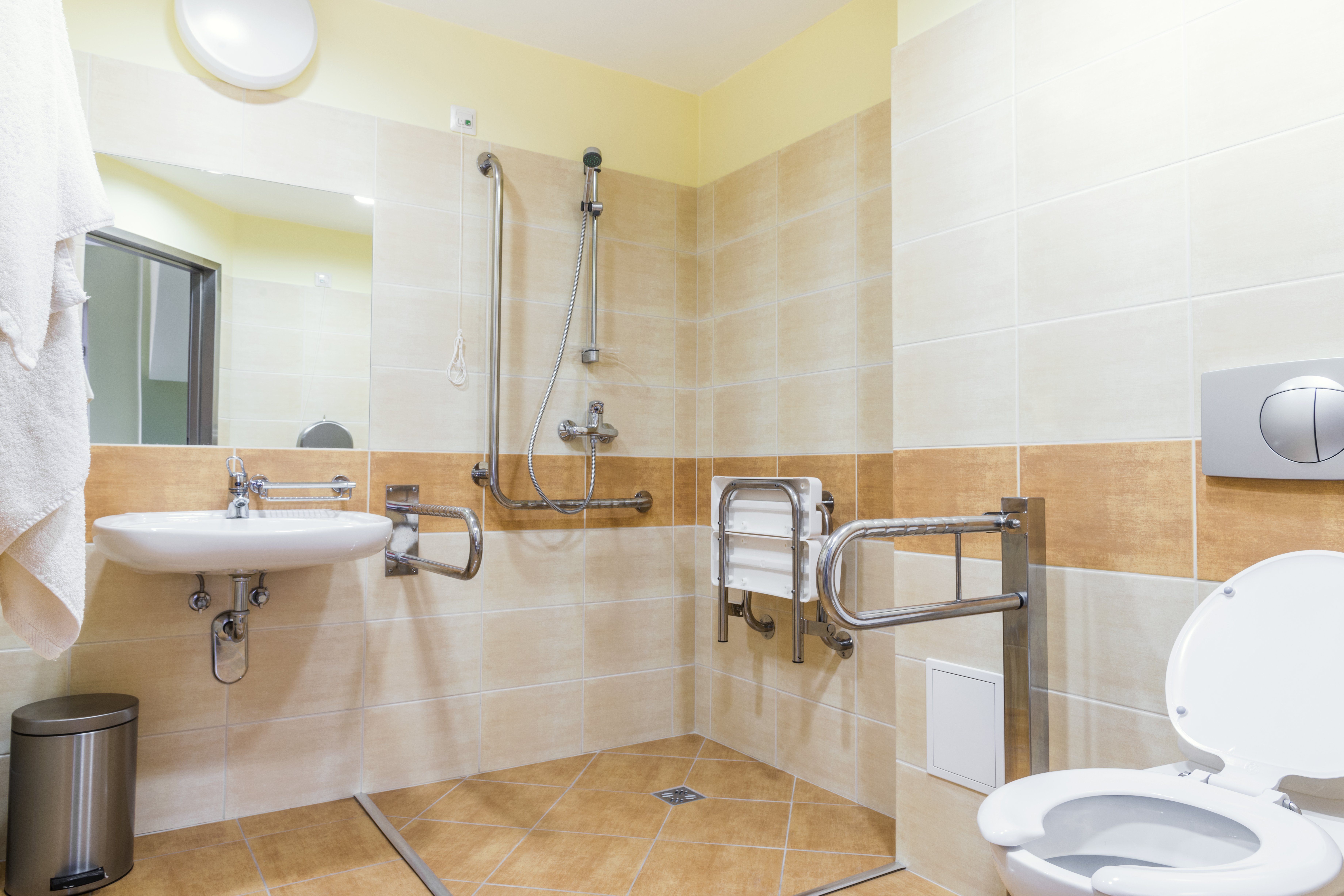 Beispiel für ein barrierefreies Bad, die Dusche ist ohne Schwelle erreichbar, direkt nebe der Toilette ist ein Haltegriff, in der Dusche gibt es eine Sitzmöglichkeit. Das Waschbecken ist unterfahrbar.