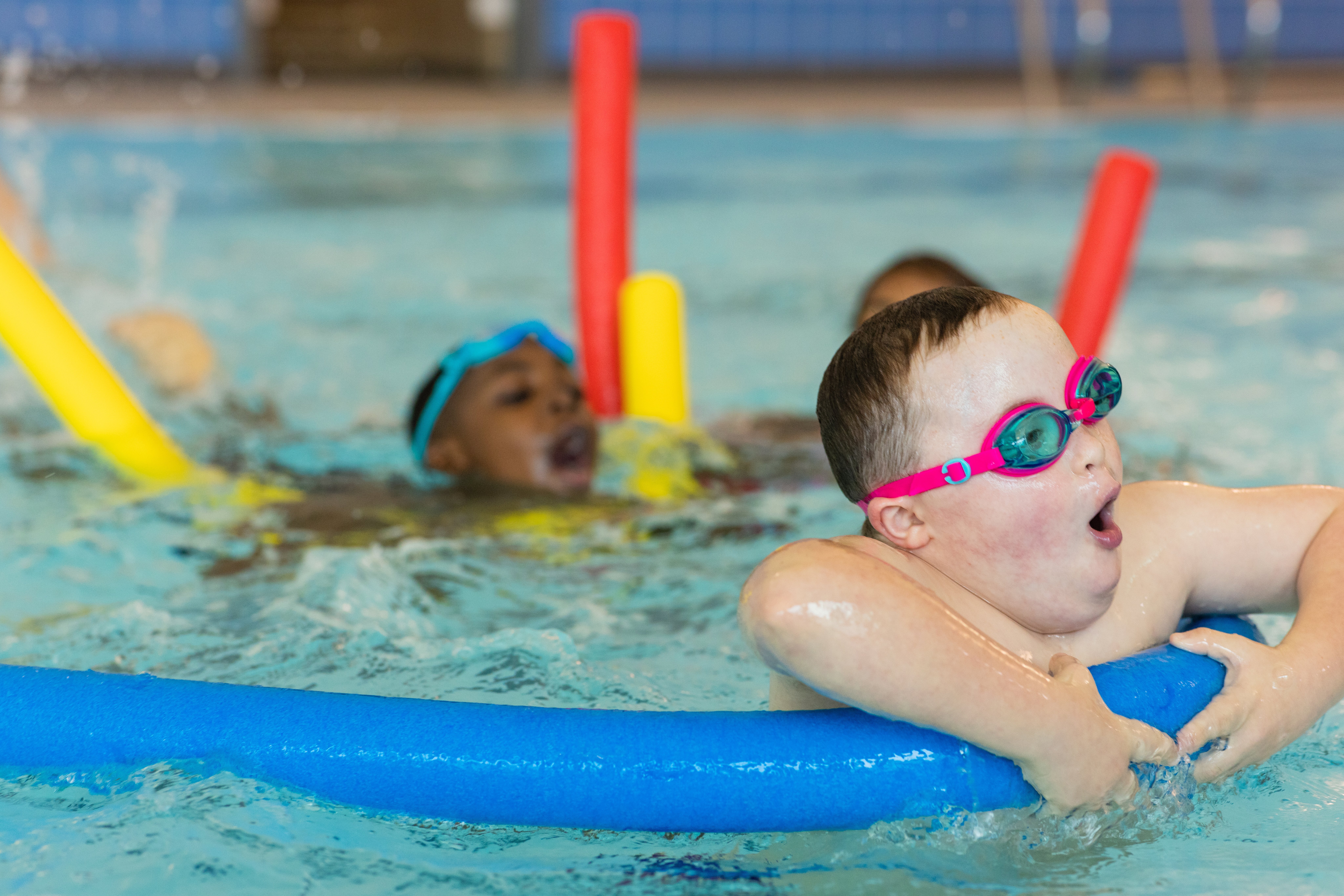 Kinder mit Behinderung schwimmen lernen Eine Gruppe von Kindern bei einem Schwimmkurs im Wasser auf Schwimmnudeln.