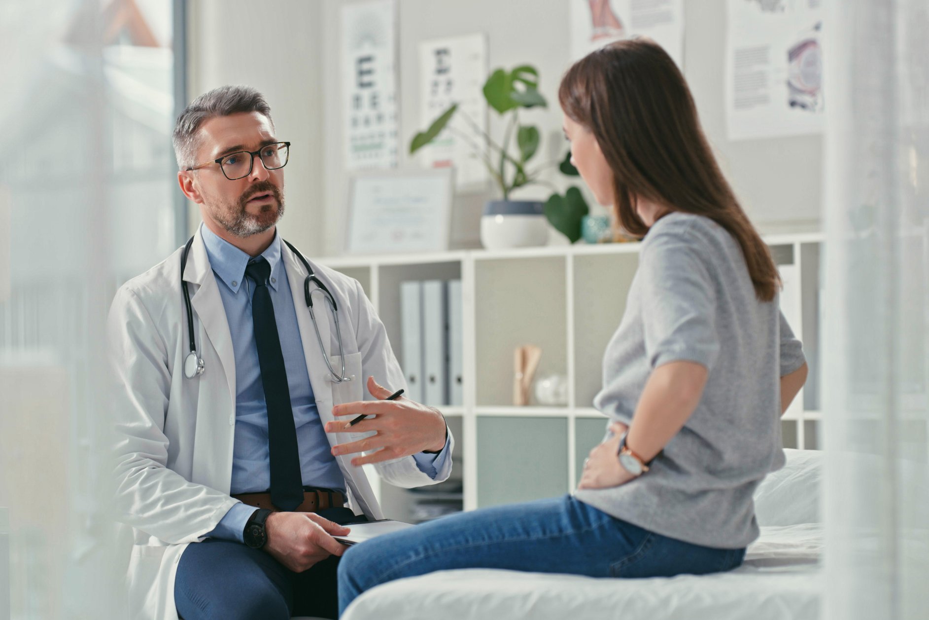 Gesetzlicher Anspruch auf Zweitmeinung Arzt sitzt mit seiner Patienten im Praxisztimmer und stellt während einer Konsultation Fragen.