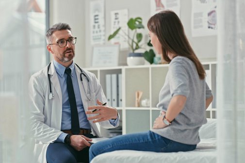 Gesetzlicher Anspruch auf Zweitmeinung Arzt sitzt mit seiner Patienten im Praxisztimmer und stellt während einer Konsultation Fragen.