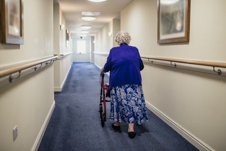 Ältere Frau geht mit Rollator einen Korridaor im Pflegeheim entlang