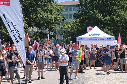 Menschen demonstrieren in Karlsruhe f&uuml;r einen starken Sozialstaat, rechts im Hintergrund ist ein wei&szlig;es Zelt, der VdK-Stand zu sehen.