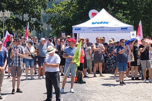 Menschen demonstrieren in Karlsruhe f&uuml;r einen starken Sozialstaat, rechts im Hintergrund ist ein wei&szlig;es Zelt, der VdK-Stand zu sehen.