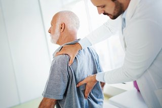 Älterer Mann beim Arzt mit Untersuchung des unteren Rückens bei Rückenschmerzen