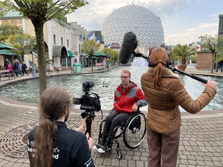 Aufnahme von den Dreharbeiten im Europa-Park, das Team fimt einen Rollstuhlfahrer, im Hintergrund ist eine Attraktion zu sehen