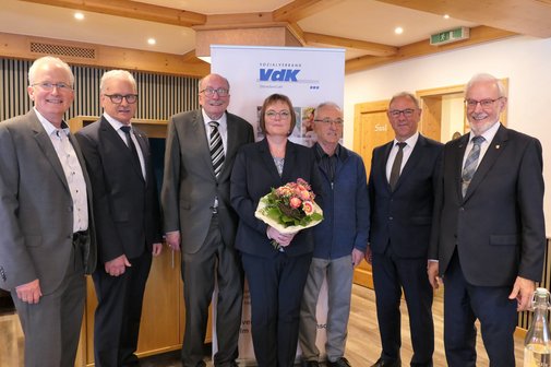 Gruppenfoto bei der Verabschiedung von Roland Hailer, die Anwesenden stehen nebeneinander und blicken in die Kamera, im Hintergrund ist das Logo des Sozialverbandes VdK auf einem Roll-Up zu sehen.