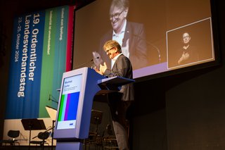 Minister Manne Lucha am Podium auf der Bühne und hält eine Rede.