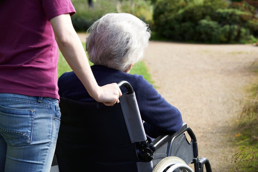 Pflegebedürftige Seniorin im Rollstuhl der von einer jüngeren Frau geschoben wird