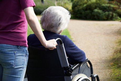 Pflegebedürftige Seniorin im Rollstuhl der von einer jüngeren Frau geschoben wird