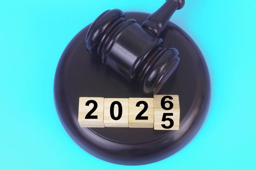 Ein Richterhammer auf blauem Hintergrund, der Richterhammer liegt auf dem Richterblock auf und trifft einen W&uuml;rfel mit der Zahl 5, der gerade am umkippen ist und zur Zahl 6 wird, mit drei weiteren Holzw&uuml;rfeln daneben bilden die W&uuml;rfel die Zahl 2026.