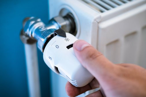 Nahaufnahme Hand schließt das Thermostatventil am Heizkörper