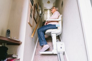 Ältere Frau sitzt auf ihrem automatischem Treppenlift auf einer Treppe in ihrem Haus