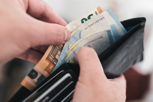 Nahaufnahme von Händen, die Euro-Scheine aus einer Brieftasche nehmen