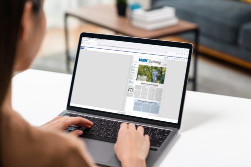 Frau sitzt am Schreibtisch an ihrem Laptop, auf dem Bildschirm ist eine Ausgabe der VdK-Zeitung zu sehen.