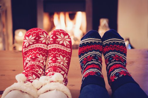 Weihnachten VdK geschlossen Kamin im Hintergrund, vorne zwei paar Füße in dicken Socken zu sehen, die ihre Füße wärmen