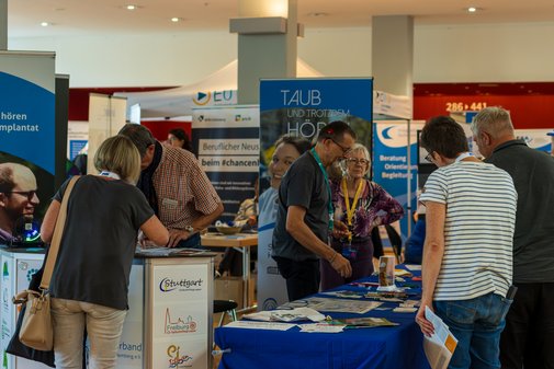 SBV-Konferenz 2025 Gesundheits- und Rehamesse Heilbronn Blick auf einen Ausstellungsstand, mehrere Personen beraten gerade Besucher.