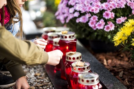 Zwei Kinder am Grab. Es gibt viele Grabkerzen in einer Reihe und eines der Kinder hält ein Blatt auf der Oberseite der Kerze. Es gibt einige Blumen im Hintergrund