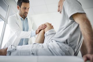 Mann auf Liege bei Krankengymnastik, Masseur behandelt das angewinkelte Knie