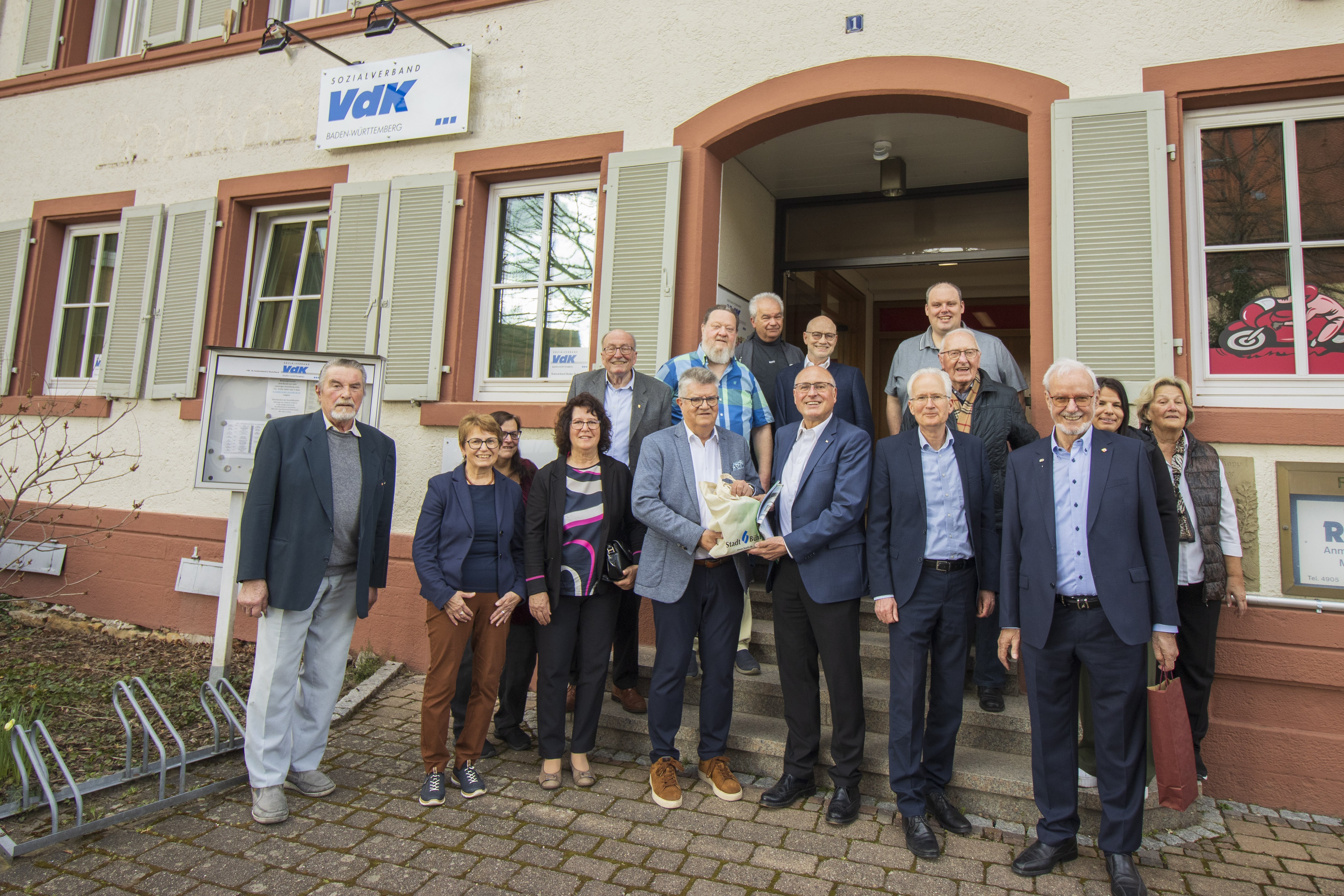 VdK-Kreisverband Baden-Baden/Bühl bezieht neue Geschäftsräume in Bühl-Kappelwindeck Außenansicht der neuen Geschäftsstelle des Kreisverbandes, vor dem Gebäude sthen die haupt- und ehrenamtlichen Mitarbeiter zusammen für ein Gruppenfoto und lache in die Kamera.