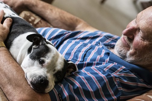Älterer Mann liegt mit seinem Hund im Arm auf dem Sofa
