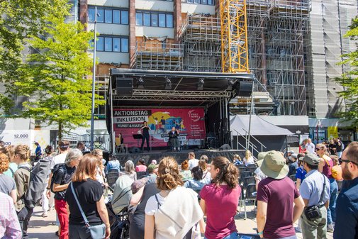 frontaler Blick auf die Bühne - dort performt gerade eine Band. Vorne im Bild sind zahlreiche Zuschauer zu sehen.