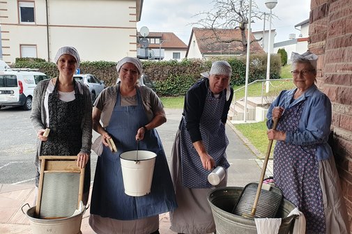 Vier Frauen posieren als "Waschweiber" vor der Kamera, mit Haatuch, Waschzuber, Waschbrett und Schwämmen.