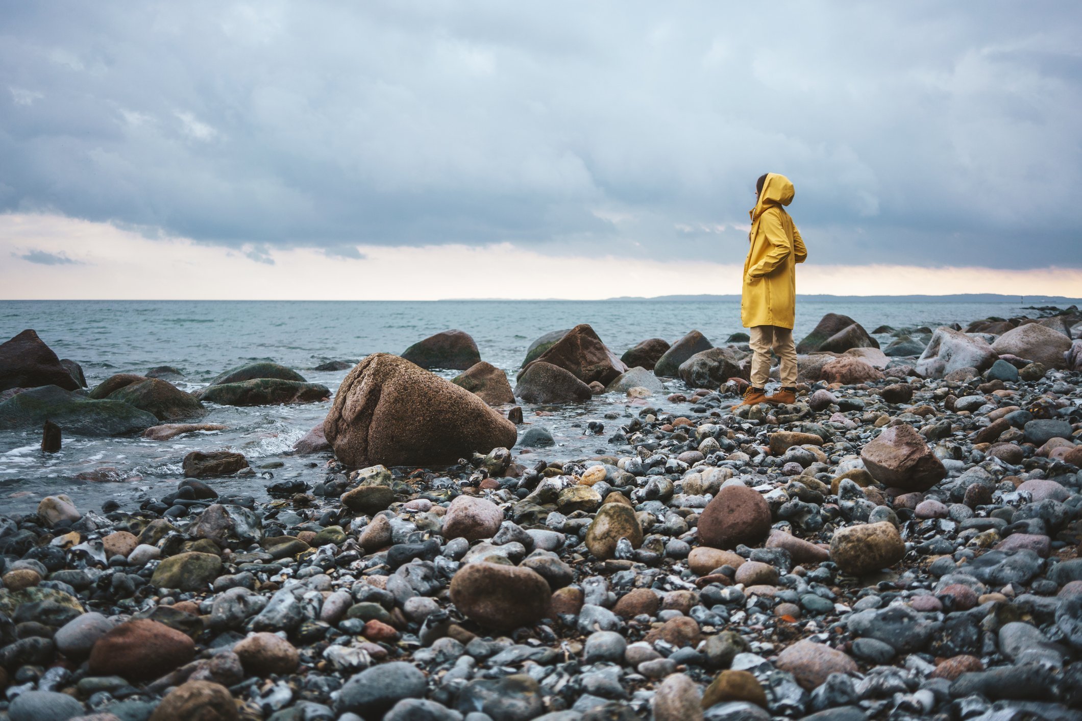 Frau mit gelbem Regenmantel, die an einem regnerischen Tag am Strand spazieren geht