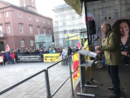 Hotz Landesvorsitzender Ansprache Renten Demo Karlsruhe Blick auf die Rednerbühne, Hans-Josef Hotz spricht zu den Anwesenden, diese blicken auf die Bühne.