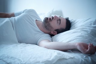 Mann schläft in seinem Bett mit geöffnetem Mund und schnauft laut