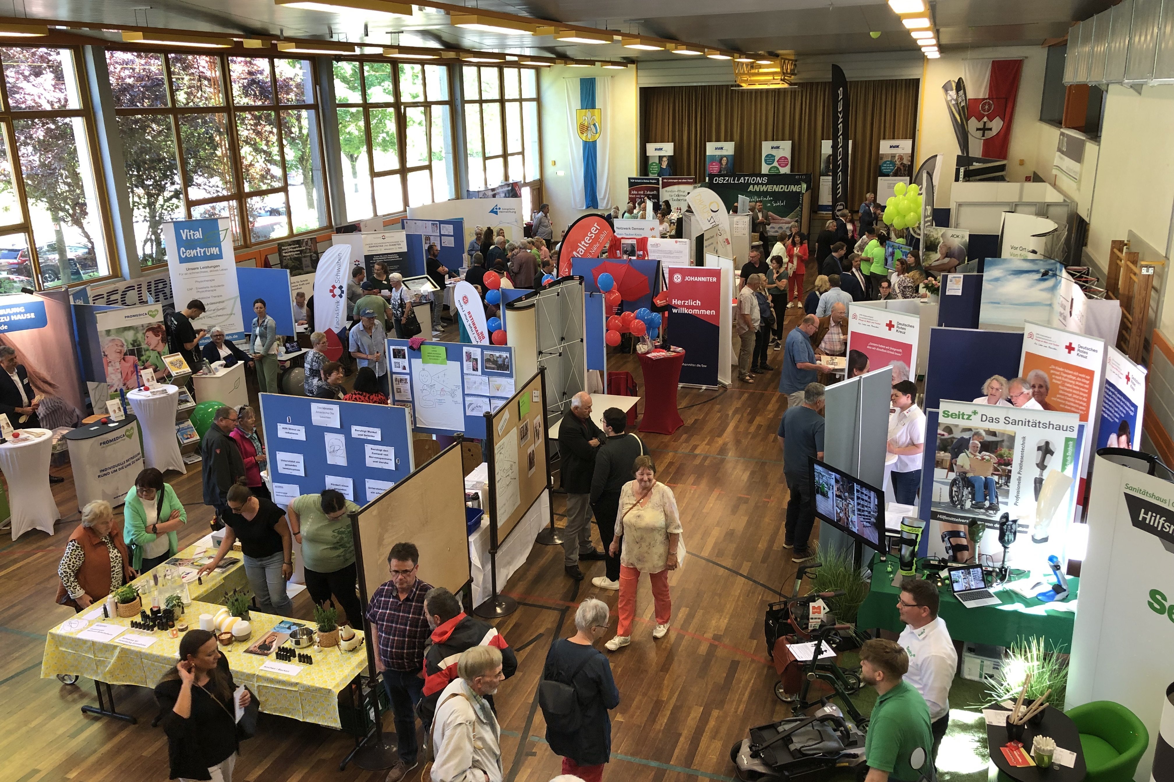 Blick von oben auf das Innere der Stadthalle Grünsfeld, aus der Vogelperspektive sieht man alle Infostände nebeneinander, die Besucher laufen zwischen den Gängen von Stand zu Stand.