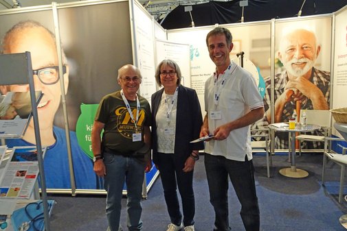 Stand auf einer Messe mit drei Personen die Besucher informieren 