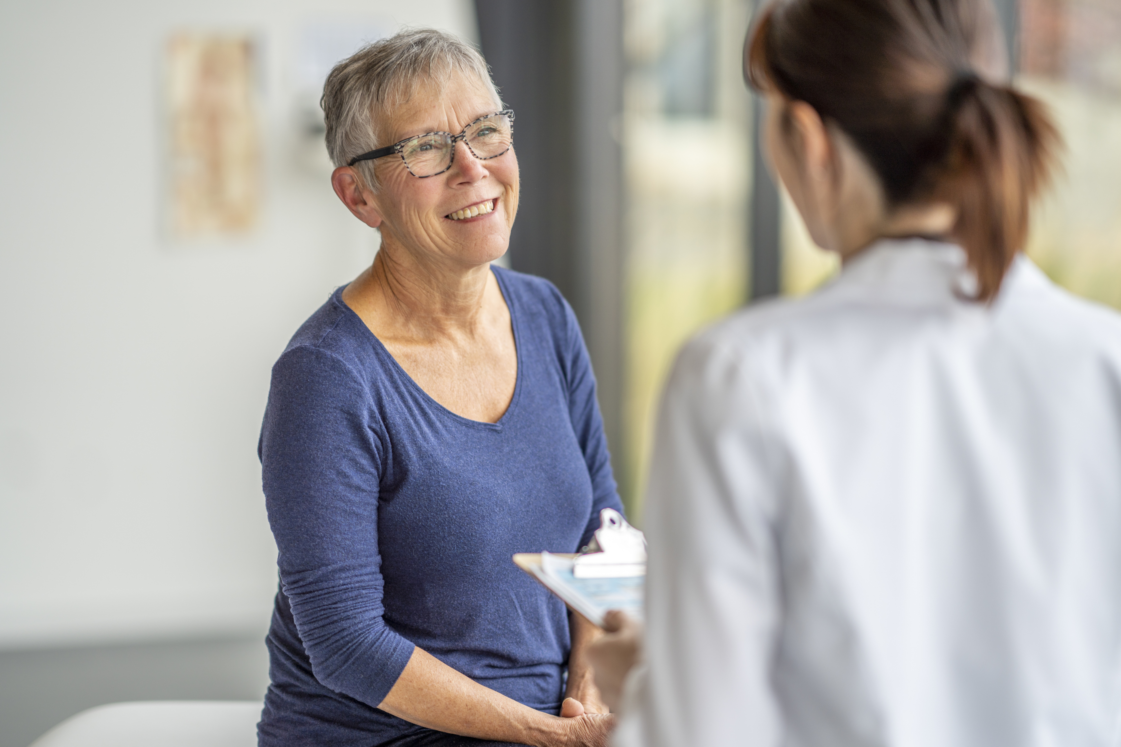 Senior bei einem Gesundheits-Check-Up beim facharzt, sie spricht mit der &Auml;rztin, diese h&auml;lt ein Klemmbret und tr&auml;gt einen wei&szlig;en Kittel.