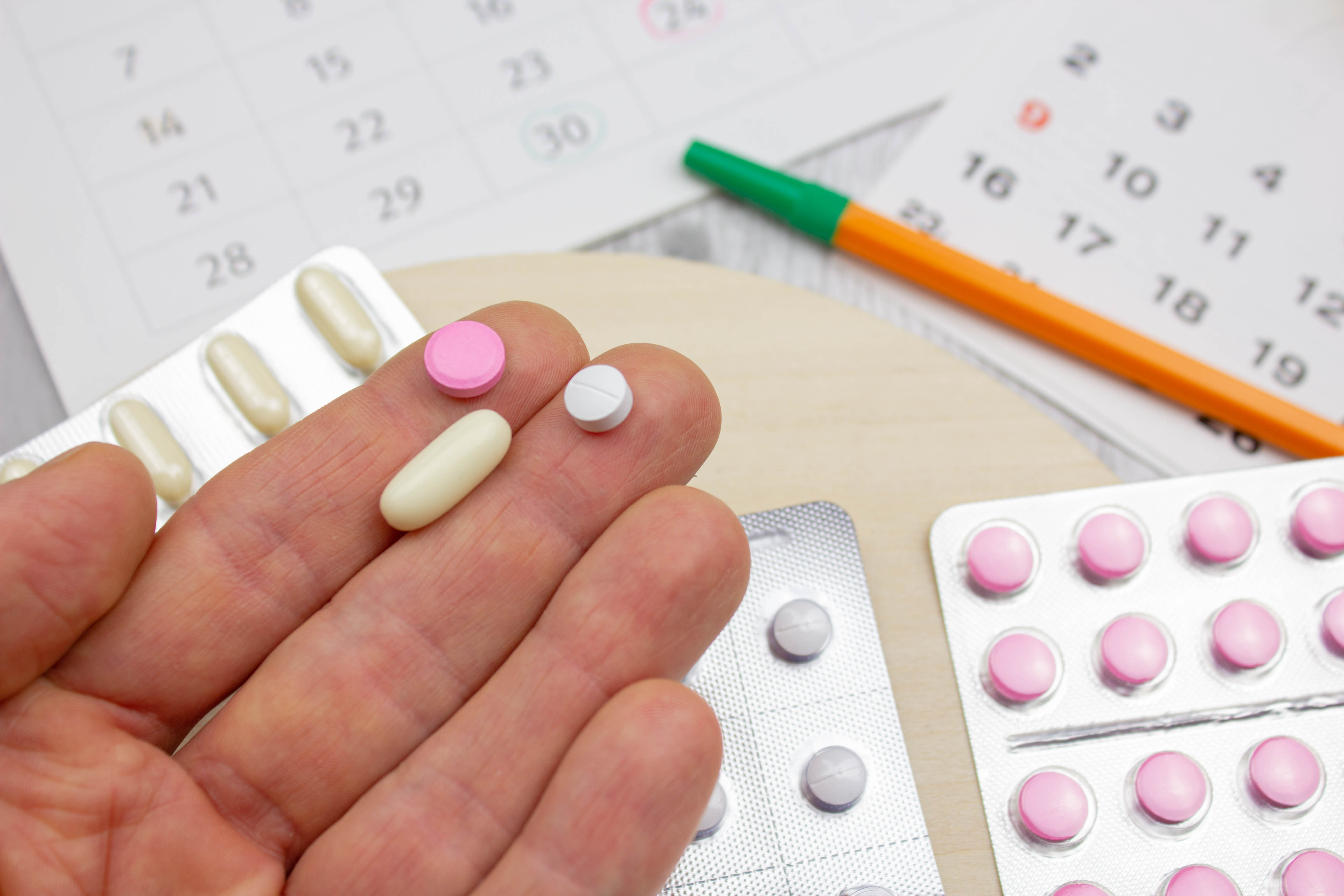 Göffnete Hand mit Tabletten darauf, auf dem Tisch darunter mehrere Tabletten