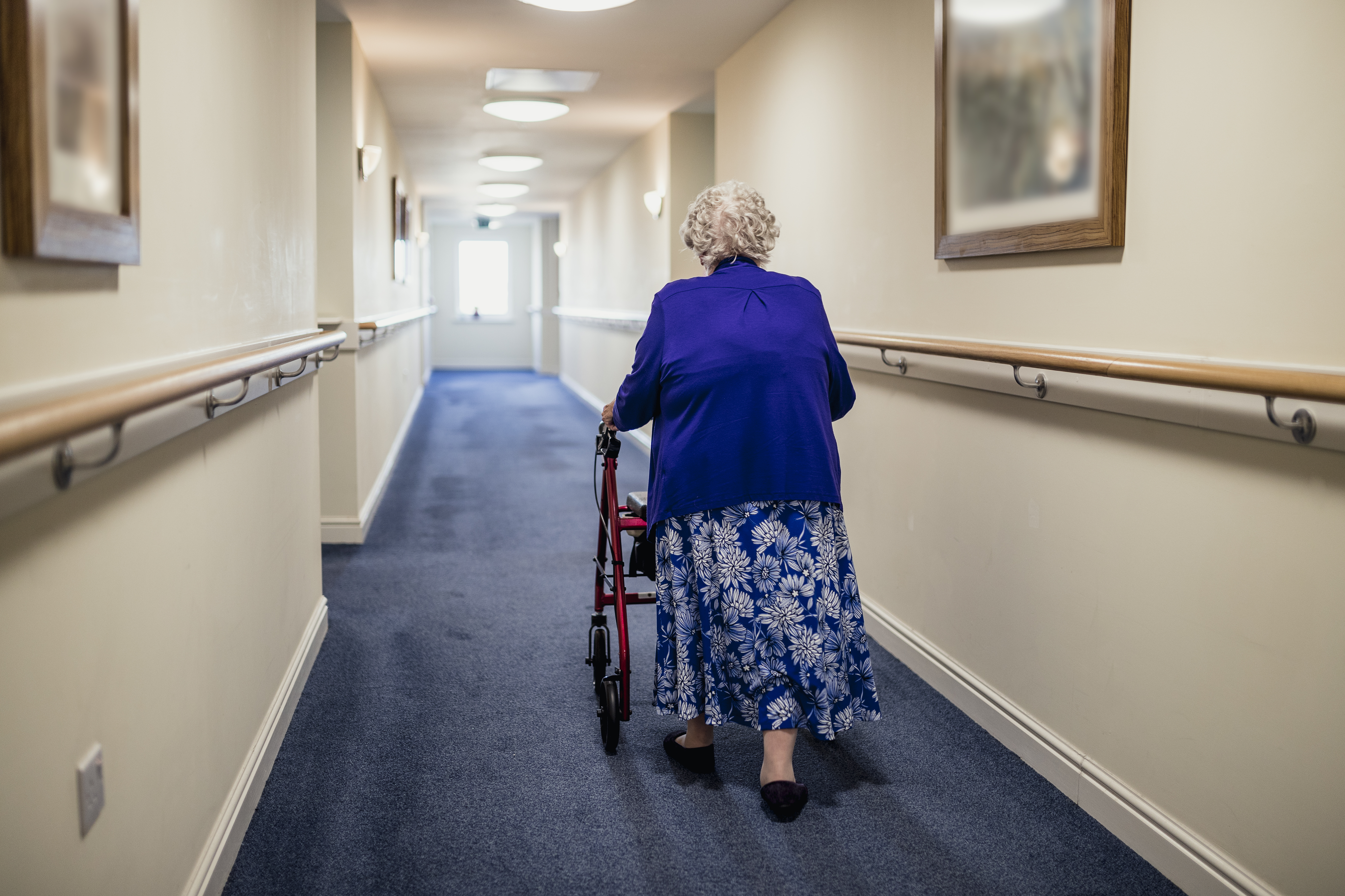 Ältere Frau geht mit Rollator einen Korridaor im Pflegeheim entlang