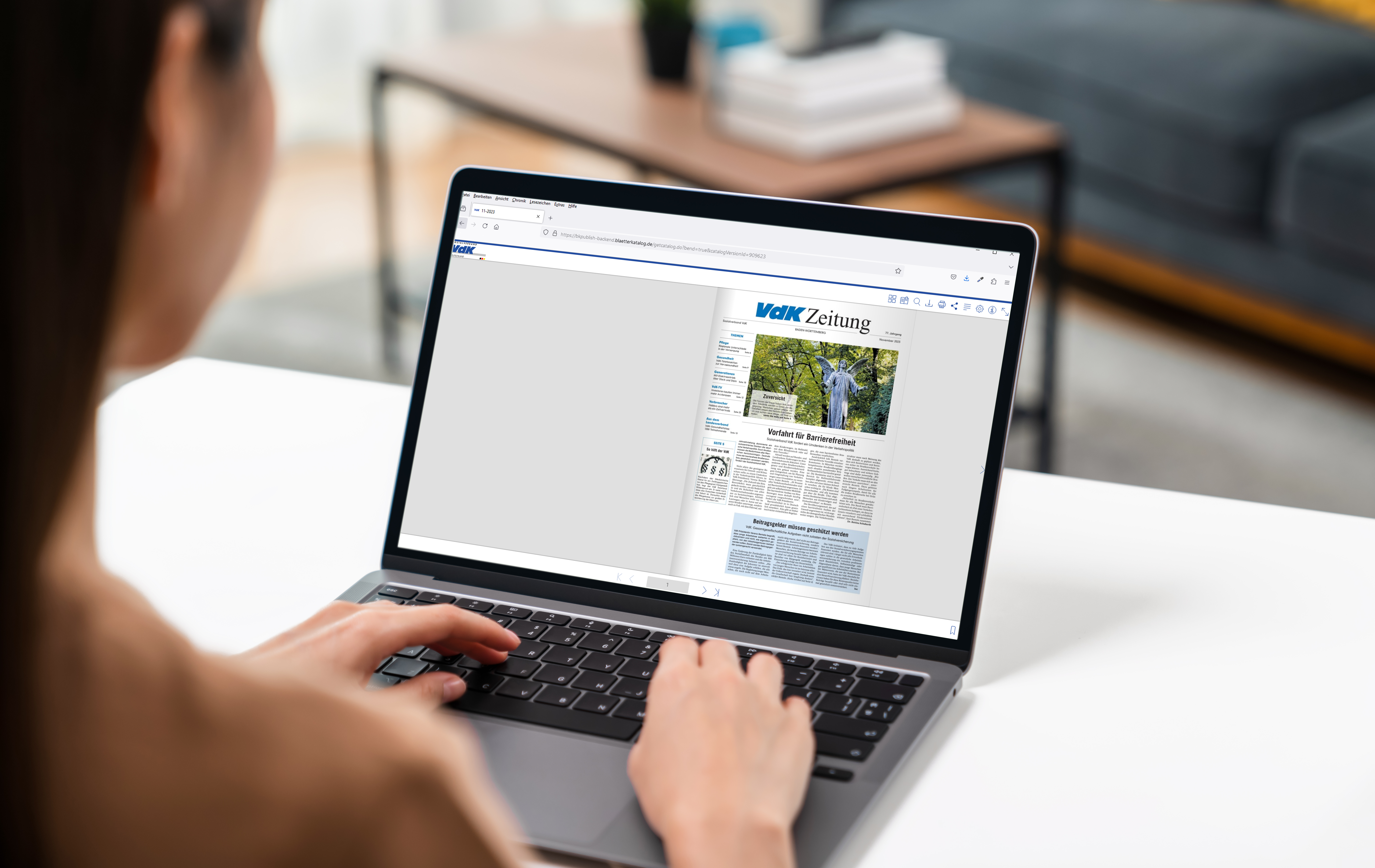 Frau sitzt am Schreibtisch an ihrem Laptop, auf dem Bildschirm ist eine Ausgabe der VdK-Zeitung zu sehen.