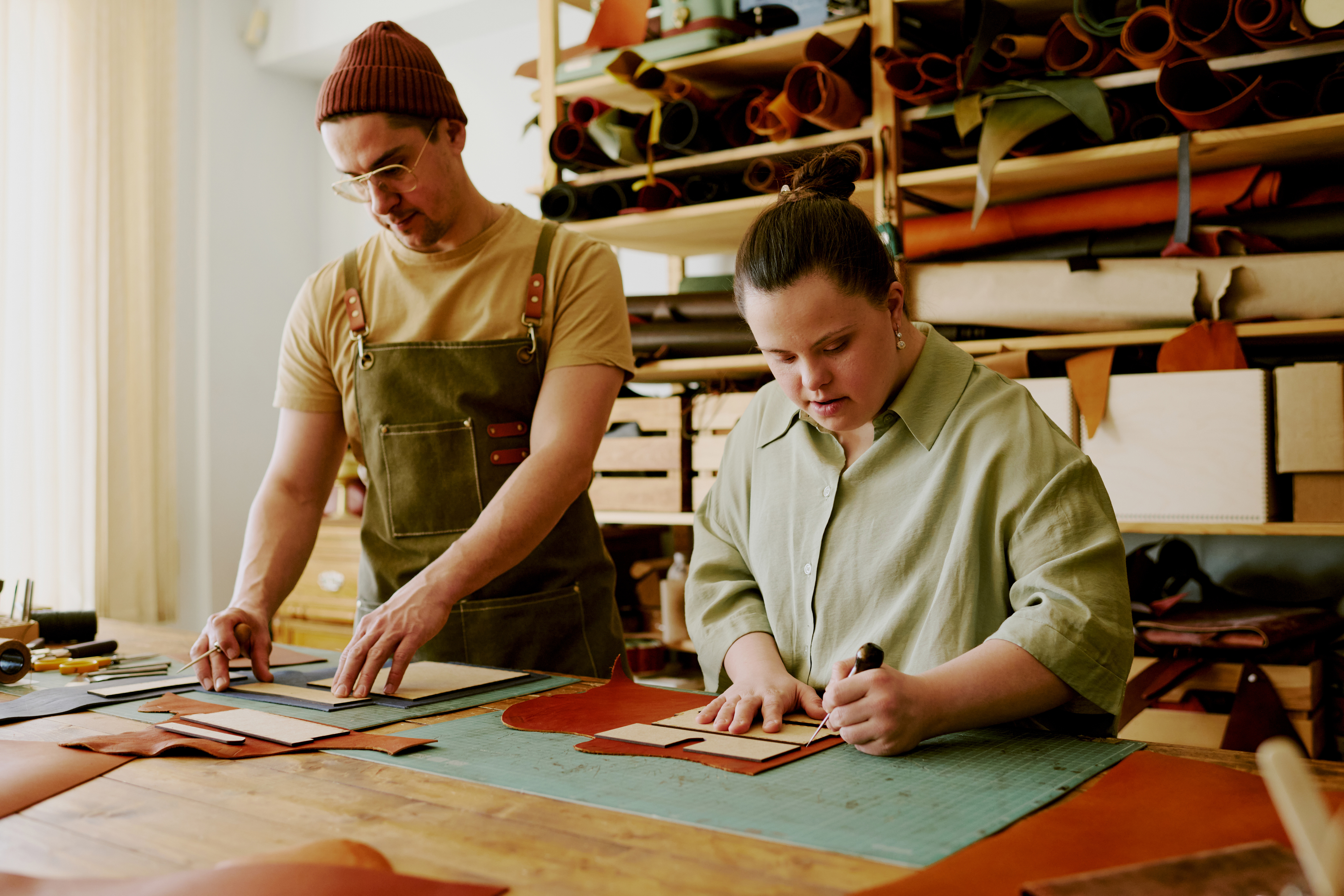 Arbeiten mit Menschen mit Behinderung Arbeit in einem Atelier, ein Mitarbeiter arbeitet mit seiner Kollegin mit Downsyndrom