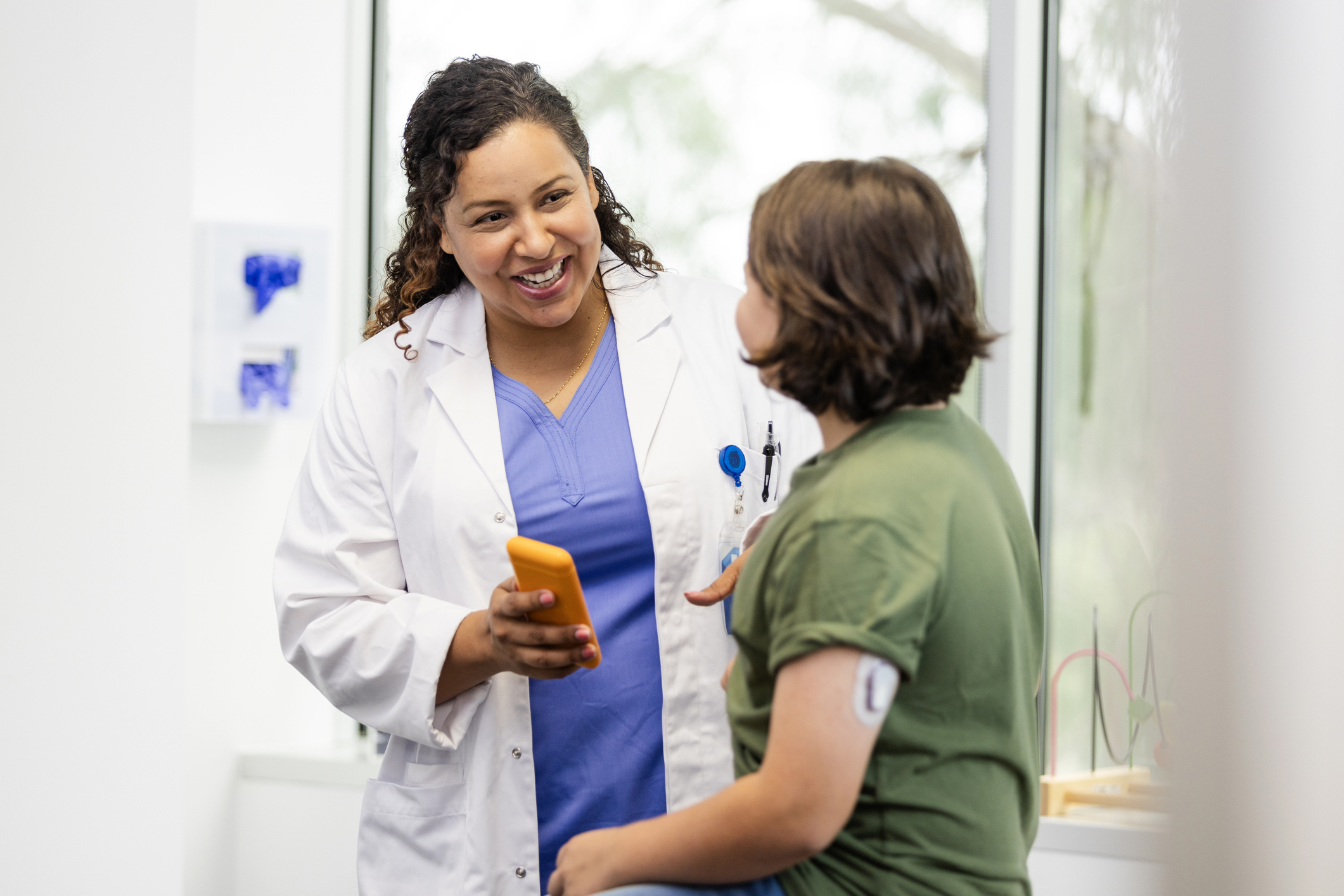 Leistungsgruppe Diabetologie Krankenhausreform Ärztin lachend im Gespräch mit einer Patientin, diese hört gespannt zu, die Ärztin hält ein Smartphone in der Hand.