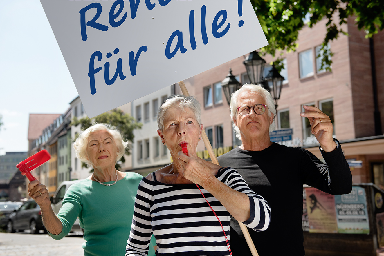 Zwei &auml;ltere Frauen und ein &auml;lterer Mann mit einer Demopappe mit der Aufschrift "Rente f&uuml;r alle!". Die Frau in der Mitte bl&auml;st in eine Trillerpfeife, die andere h&auml;lt eine Ratsche in der Hand. 