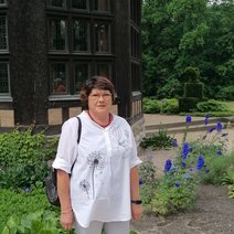 Eine Frau steht vor einem Holzpavillion und blickt freundlich in die Kamera
