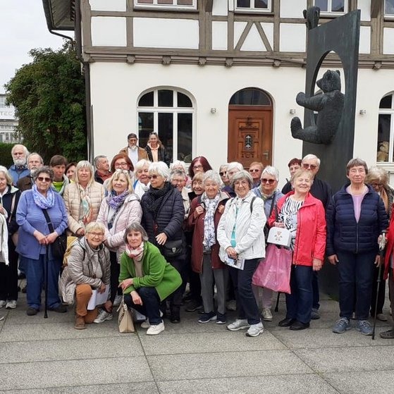 VdK OV Hochdorf Gruppenbild mit etwa 40 älteren Menschen vor einem gusseisernen Denkmal mit einem Teddybär.